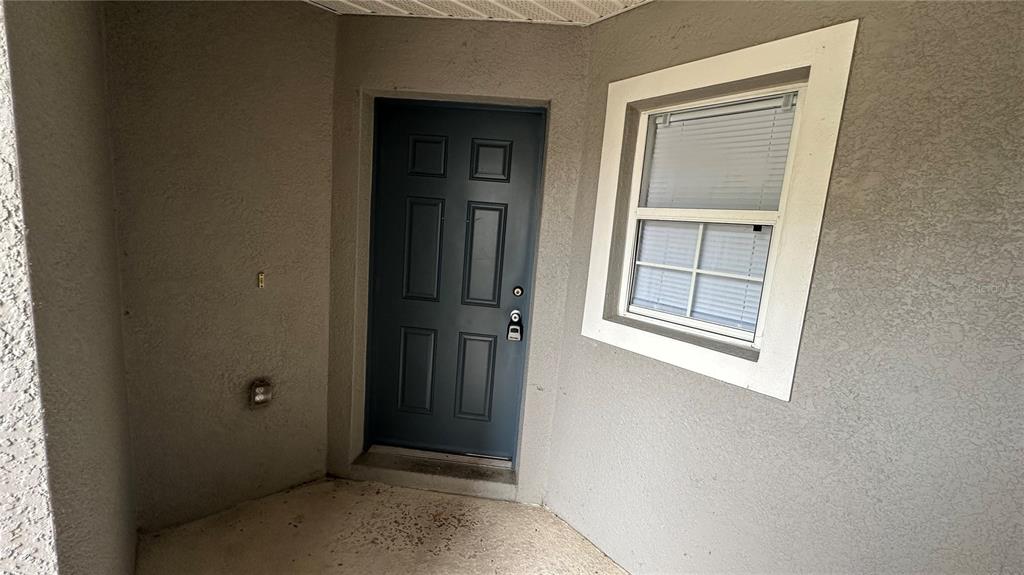 A gray front door and a window with white trim are set in a stucco entryway — 2437 HASSONITE STREET, KISSIMMEE, FL