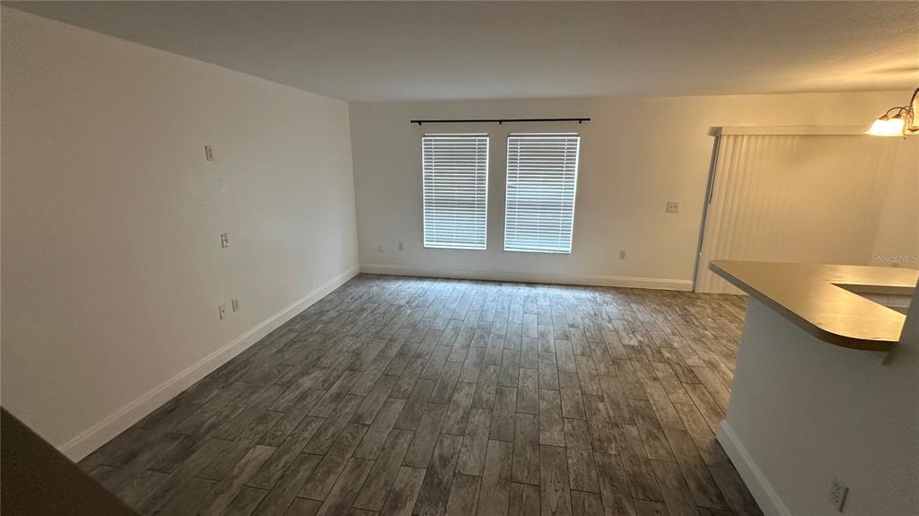 An empty living room features wood-look tile flooring, white walls, and a sliding glass door — 2437 HASSONITE STREET, KISSIMMEE, FL