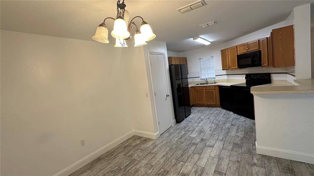 A dining area with a chandelier leads into a kitchen featuring wood cabinets and appliances — 2437 HASSONITE STREET, KISSIMMEE, FL