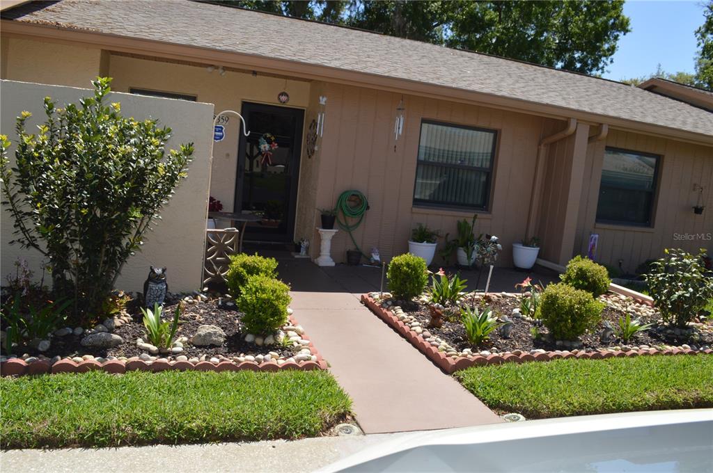 A tan single-story house features a concrete walkway leading to a front entrance with landscaping — 38359 IRONWOOD PLACE UNIT 0, ZEPHYRHILLS, FL