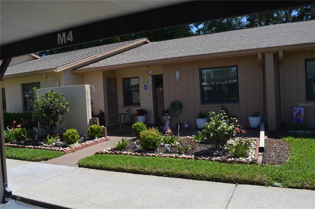A single-story residential unit features a covered entryway, a small front garden, and a carport — 38359 IRONWOOD PLACE UNIT 0, ZEPHYRHILLS, FL