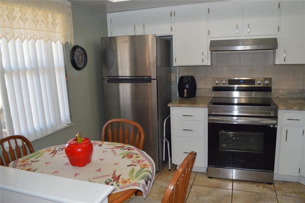 A kitchen features white cabinets, stainless steel appliances, tile flooring, and a small dining table — 38359 IRONWOOD PLACE UNIT 0, ZEPHYRHILLS, FL