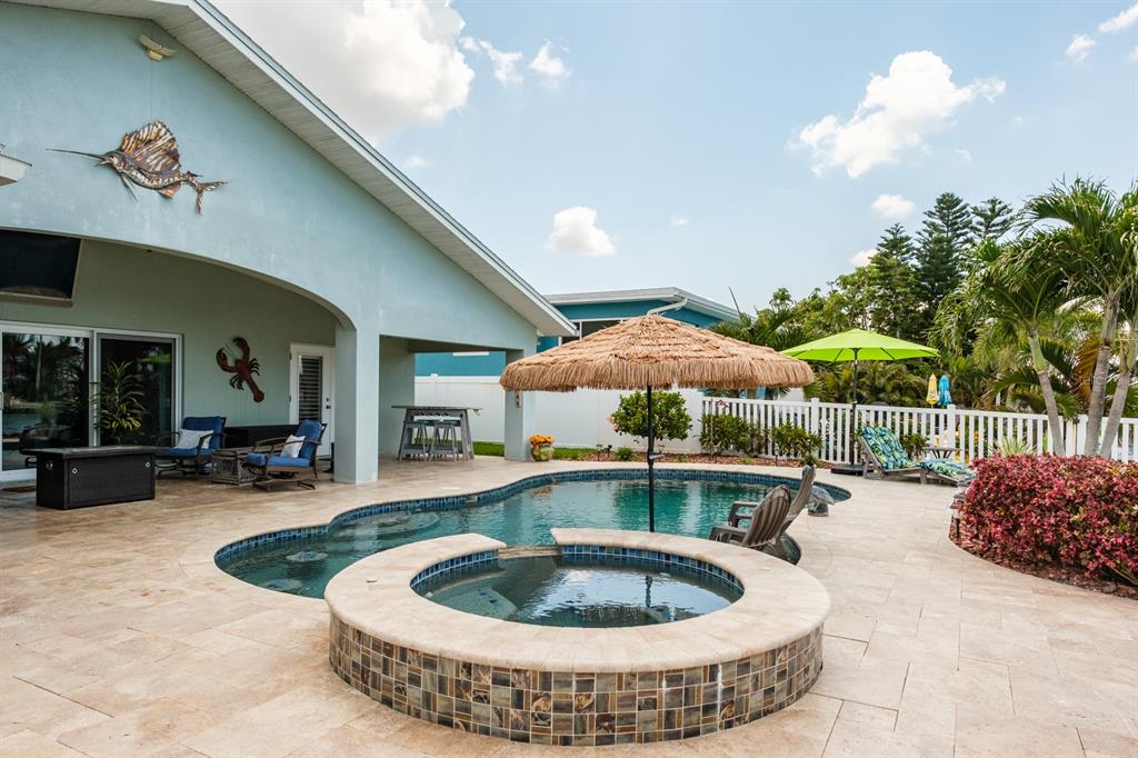A backyard features a swimming pool, a raised hot tub, and a covered patio area — 11400 8TH STREET E, TREASURE ISLAND, FL