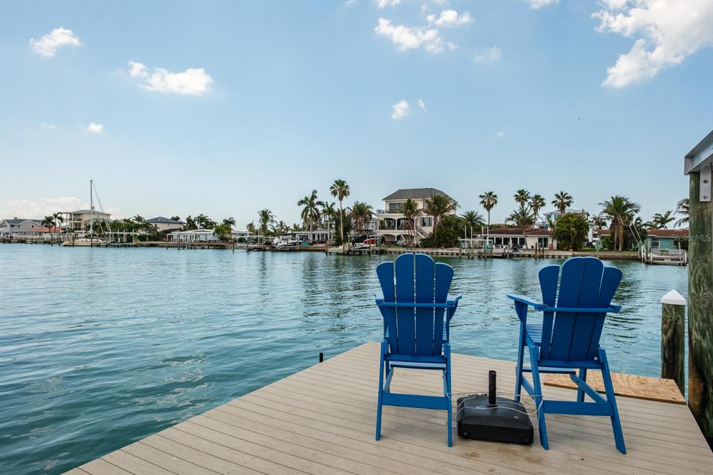 Two blue Adirondack chairs sit on a wooden dock overlooking a calm canal and houses — 11400 8TH STREET E, TREASURE ISLAND, FL