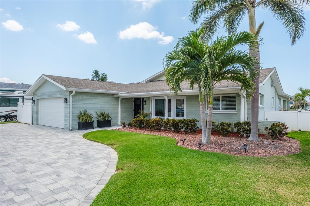 A light green brick house with a paved driveway, palm trees, and a grassy lawn — 11400 8TH STREET E, TREASURE ISLAND, FL