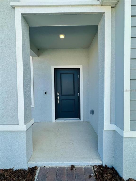 A covered entryway features a dark blue front door with a smart lock and light — 2665 ARMSTRONG AVENUE, CLERMONT, FL
