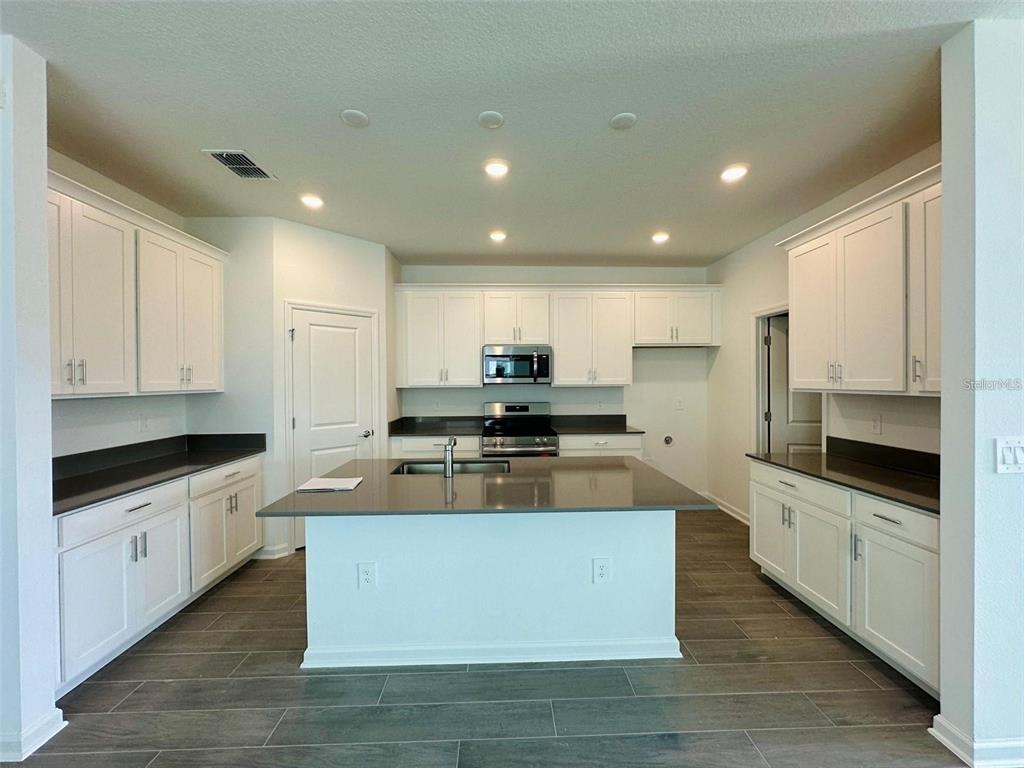A kitchen features white cabinets, dark countertops, a central island, and wood-look tile flooring — 2665 ARMSTRONG AVENUE, CLERMONT, FL