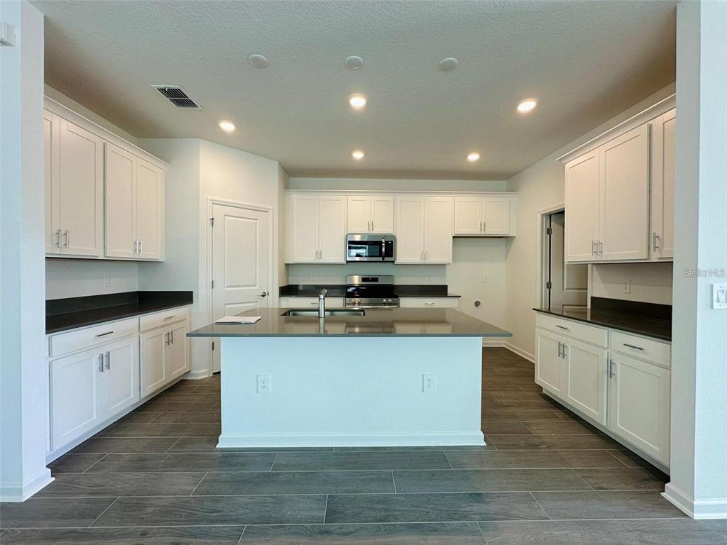 A kitchen features white cabinets, a central island with a sink, and dark countertops — 2665 ARMSTRONG AVENUE, CLERMONT, FL