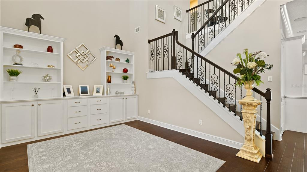 A foyer features a staircase with iron railings, built-in white shelving, and dark wood flooring — 14240 COLONIAL POINTE DRIVE, WINTER GARDEN, FL