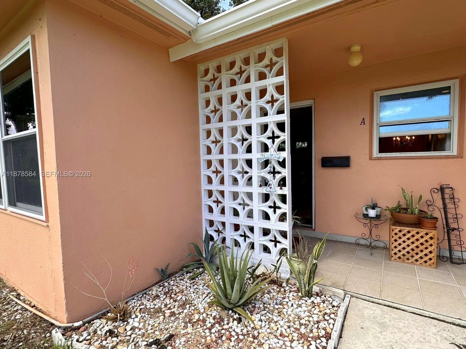 The exterior of a house features a peach-colored wall, a decorative breeze block screen, and landscaping — 285 N High Point Blvd # A, Boynton Beach FL 33435, BOYNTON BEACH, FL