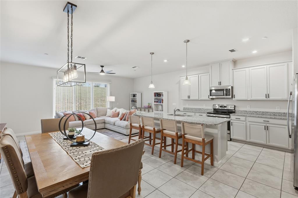 An open-concept kitchen and dining area features white cabinetry, granite countertops, and tile flooring — 1788 HOLDEN RIDGE LANE, MINNEOLA, FL