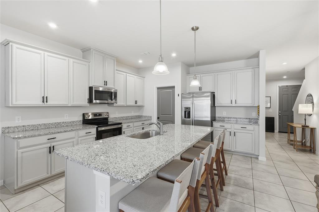A kitchen features white cabinets, granite countertops, a central island with seating, and stainless appliances — 1788 HOLDEN RIDGE LANE, MINNEOLA, FL