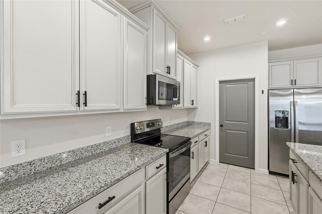 A kitchen features light gray cabinets, granite countertops, stainless steel appliances, and tile flooring — 1788 HOLDEN RIDGE LANE, MINNEOLA, FL
