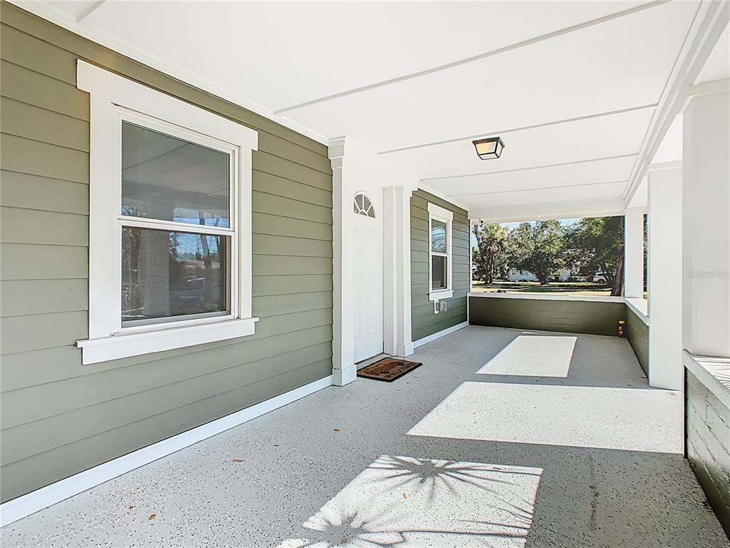 A covered front porch with olive green siding, a white door, and a speckled floor — 1223 SYCAMORE STREET, LAKELAND, FL