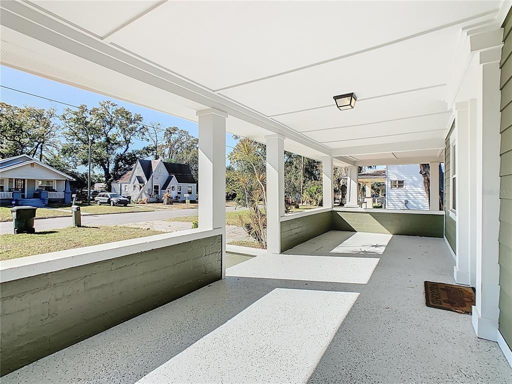 A covered front porch features a concrete floor, green half-walls, and white support columns — 1223 SYCAMORE STREET, LAKELAND, FL