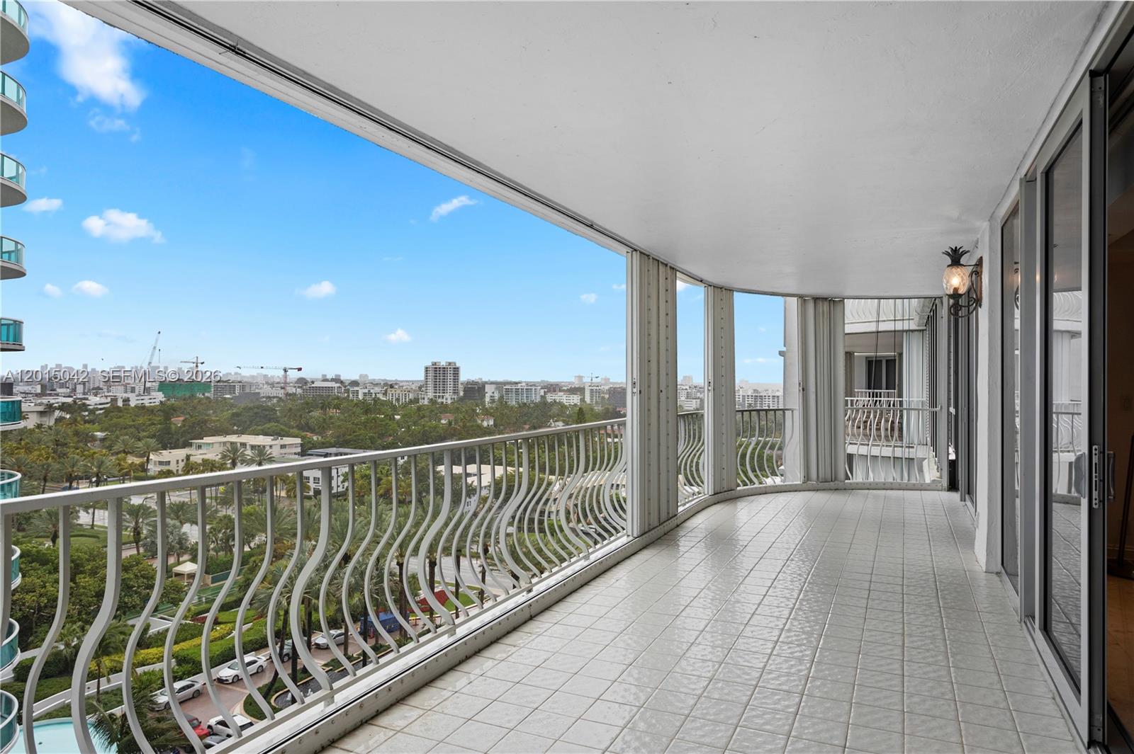 A tiled balcony with a curved white railing overlooks a city skyline and lush trees — 10155 Collins Ave # 1105, Bal Harbour FL 33154, BAL HARBOUR, FL