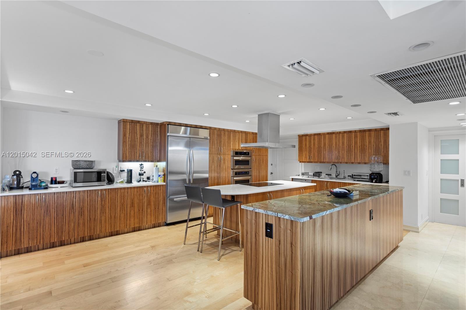 A modern kitchen features wood-grain cabinetry, stainless steel appliances, and two large kitchen islands — 10155 Collins Ave # 1105, Bal Harbour FL 33154, BAL HARBOUR, FL