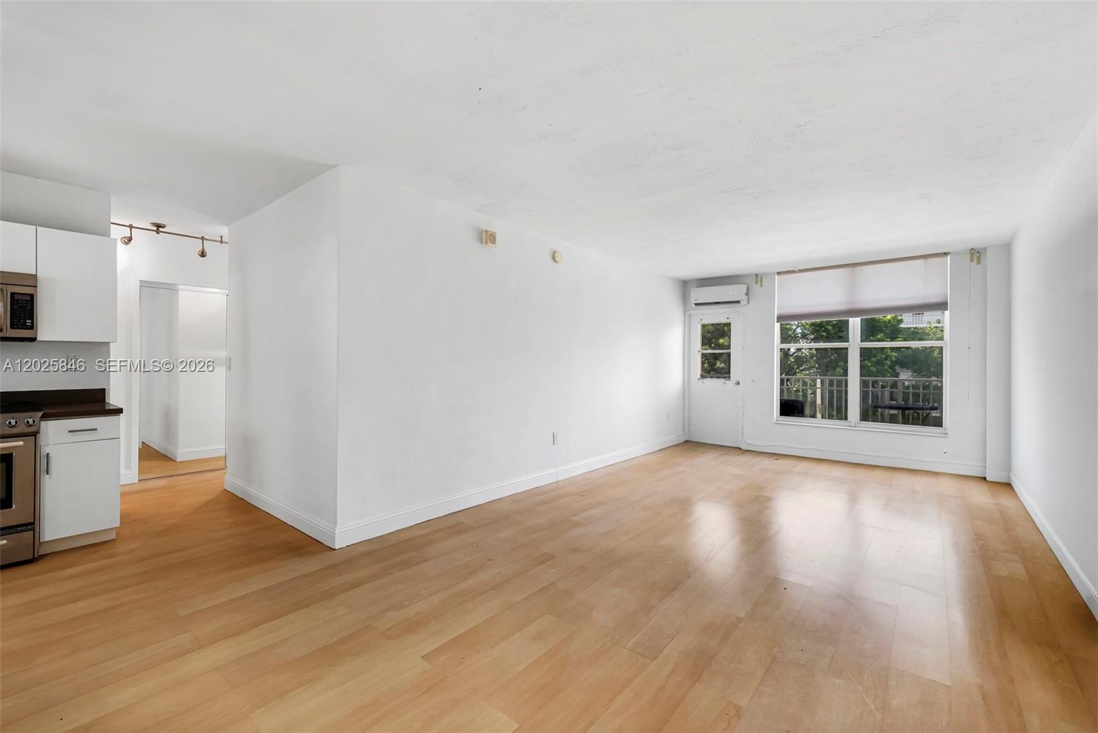 An open-plan living area features light wood flooring, white walls, and an adjacent kitchen — 1300 Lincoln Rd # B402, Miami Beach FL 33139, MIAMI BEACH, FL