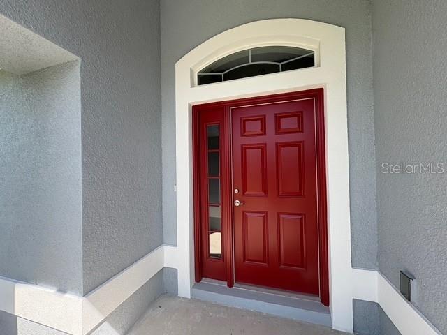 A red front door with a side light and arched transom window sits in a entryway — 165 MARION OAKS PASS, OCALA, FL