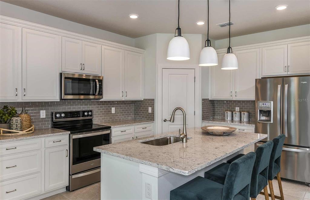 A kitchen features white cabinets, granite countertops, a gray tile backsplash, and a center island — 6918 SW 90TH LANE, OCALA, FL