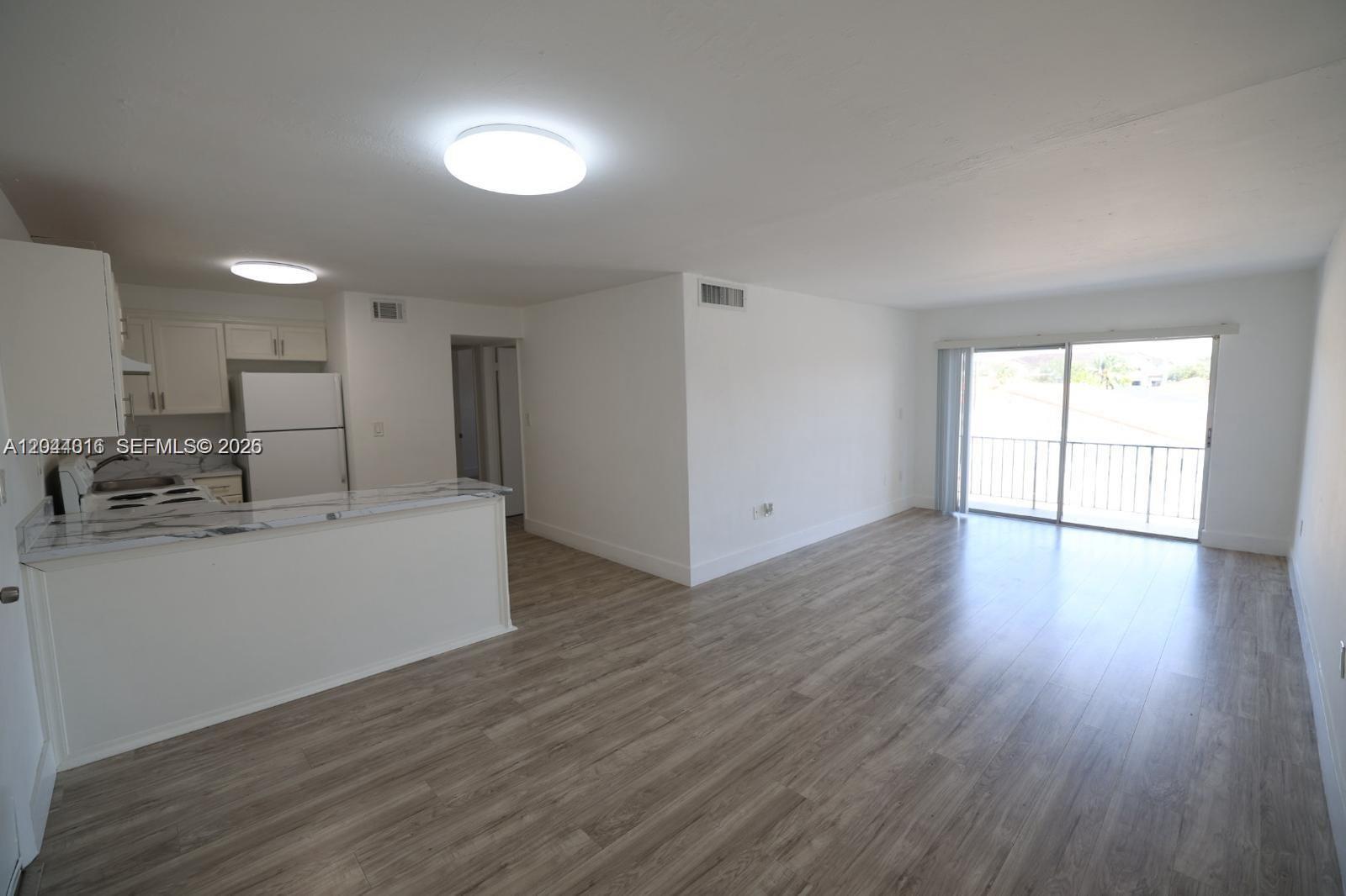An open-concept living room features wood-look flooring, a kitchen with white cabinets, and a balcony — 3501 W 11th Ave # 202, Hialeah FL 33012, HIALEAH, FL