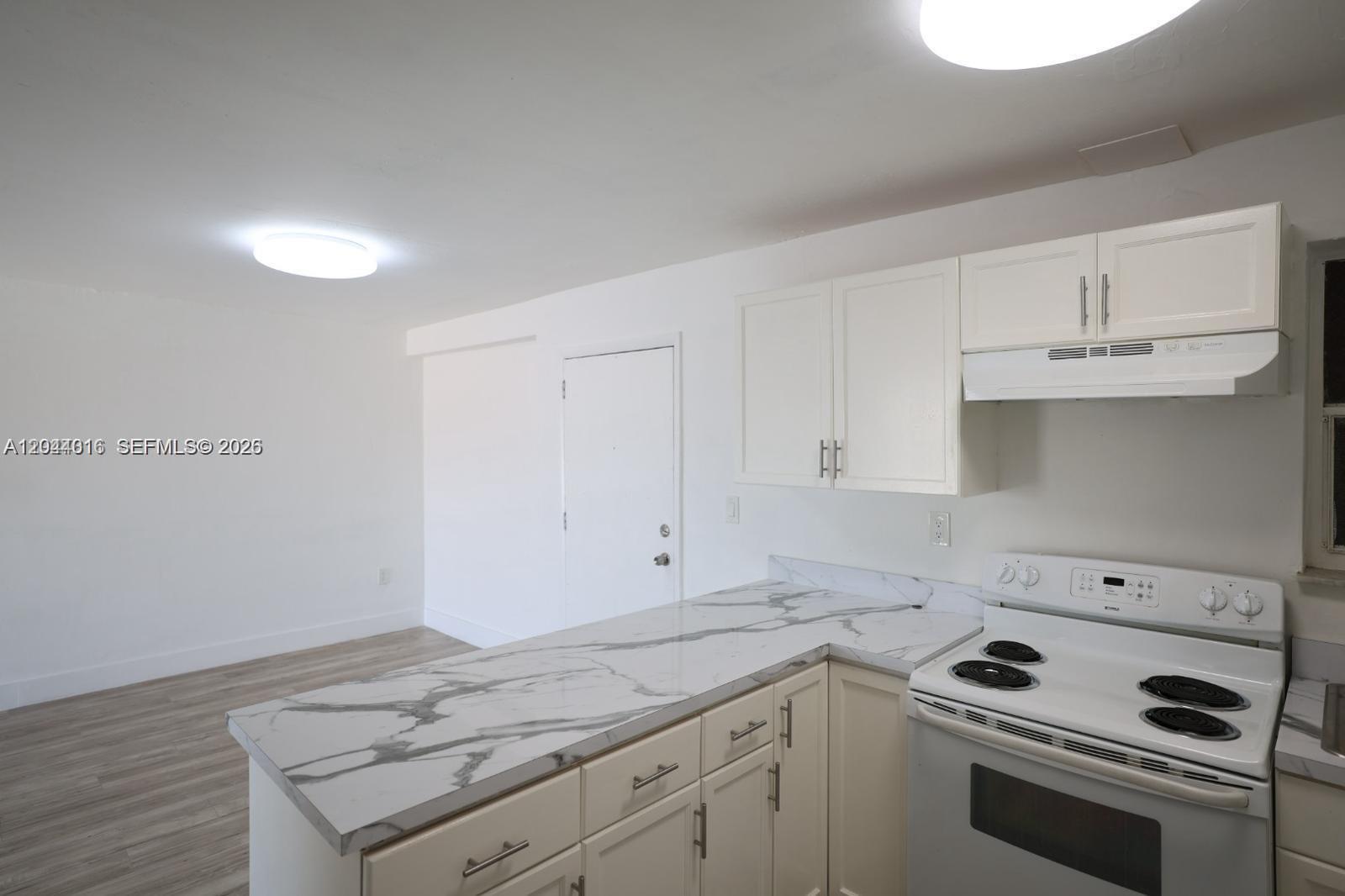 A kitchen features white cabinets, a marble-patterned countertop, and a white electric range — 3501 W 11th Ave # 202, Hialeah FL 33012, HIALEAH, FL