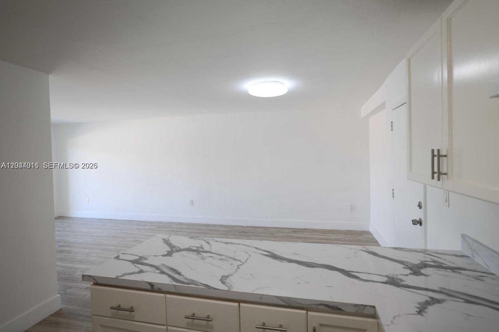 A kitchen counter with a marble-patterned top overlooks an empty, white-walled living area — 3501 W 11th Ave # 202, Hialeah FL 33012, HIALEAH, FL