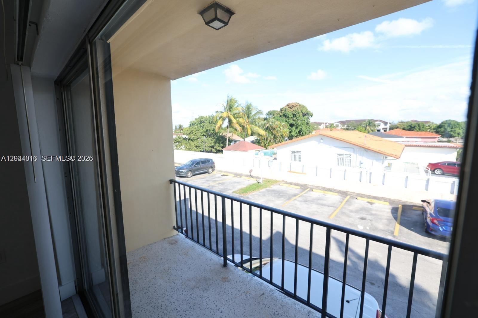 A balcony with a black metal railing overlooks a parking lot and nearby residential buildings — 3501 W 11th Ave # 202, Hialeah FL 33012, HIALEAH, FL