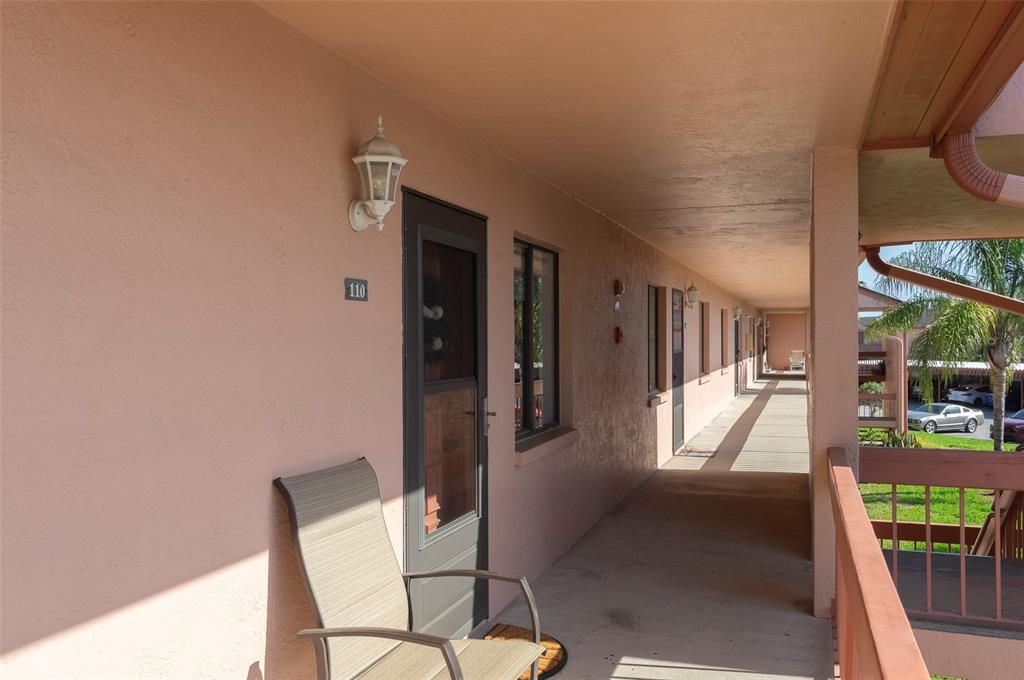 An exterior walkway features a row of apartment doors, a chair, and a metal railing — 110 LAKESIDE COURT UNIT 110, OLDSMAR, FL