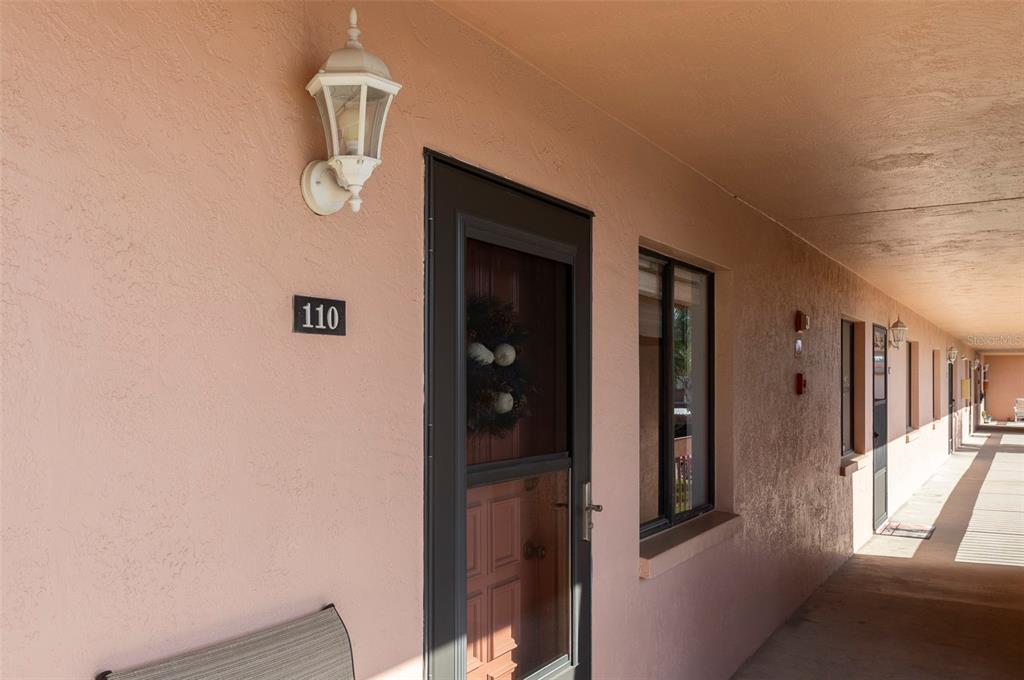 A covered outdoor walkway leads to the entrance of unit 110 with a storm door — 110 LAKESIDE COURT UNIT 110, OLDSMAR, FL
