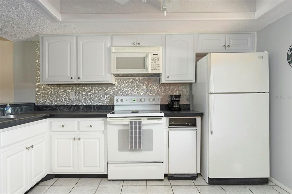 A kitchen with white cabinets, a white stove, a white refrigerator, and a metallic backsplash — 110 LAKESIDE COURT UNIT 110, OLDSMAR, FL