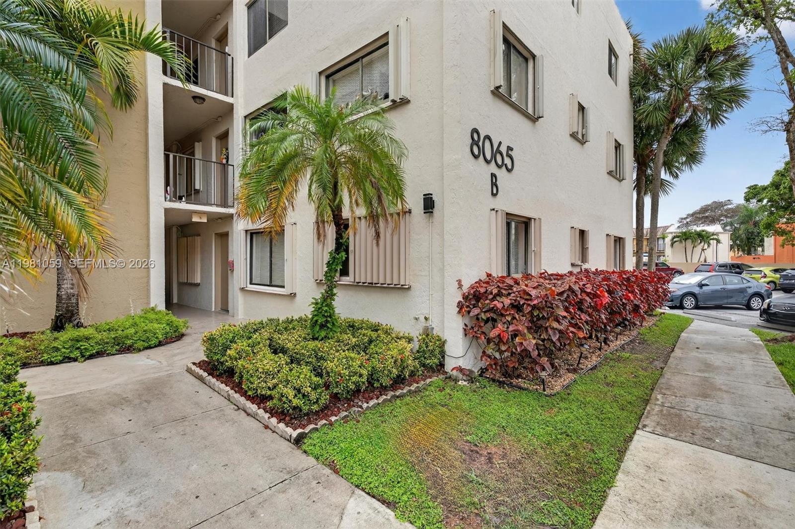 The exterior of a multi-story apartment building features a palm tree and landscaped garden beds — 8065 SW 107th Ave # 106, Miami FL 33173, MIAMI, FL