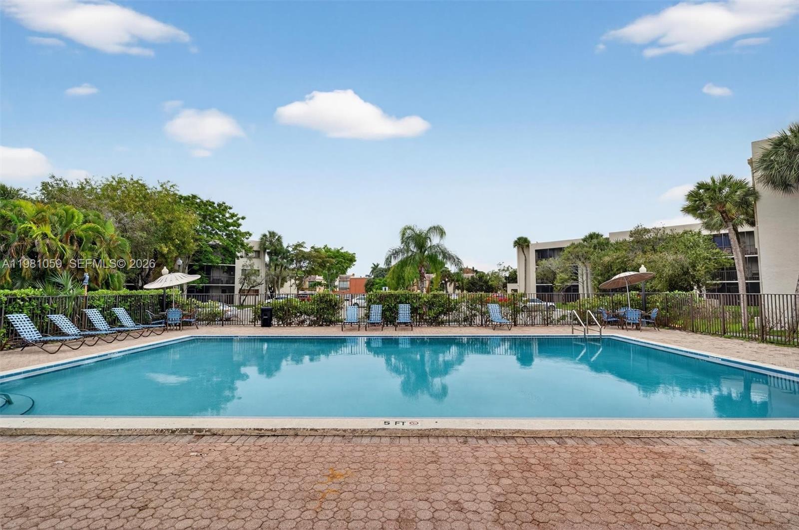 A rectangular outdoor swimming pool is surrounded by lounge chairs, umbrellas, and a metal fence — 8065 SW 107th Ave # 106, Miami FL 33173, MIAMI, FL