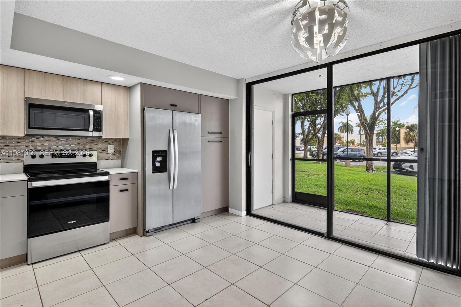 A kitchen with stainless steel appliances and tile flooring opens to a screened-in patio — 8065 SW 107th Ave # 106, Miami FL 33173, MIAMI, FL