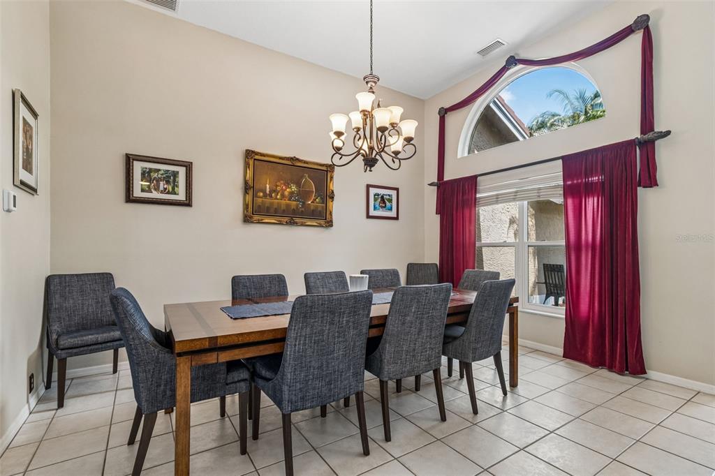 A dining room features a wooden table, gray chairs, a chandelier, and tall red curtains — 2937 HILLCREEK CIRCLE S, CLEARWATER, FL