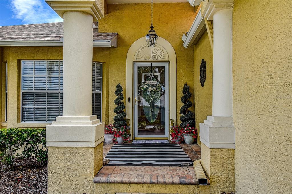 A yellow house exterior features a front porch with two white columns and a door — 18624 GRAND CLUB DRIVE, HUDSON, FL