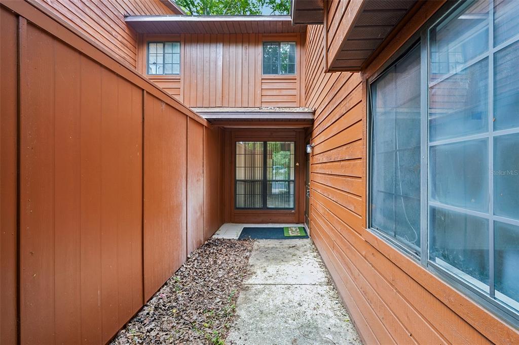 A concrete walkway leads to the front entrance of a house with brown wood siding — 5606 SW 8TH PLACE, GAINESVILLE, FL