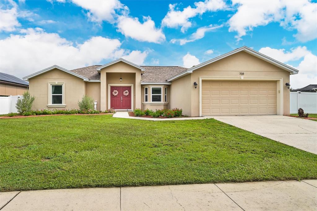 A single-story house with a tan stucco exterior, a two-car garage, and a red front door — 708 TOWER GROVE DRIVE, PLANT CITY, FL