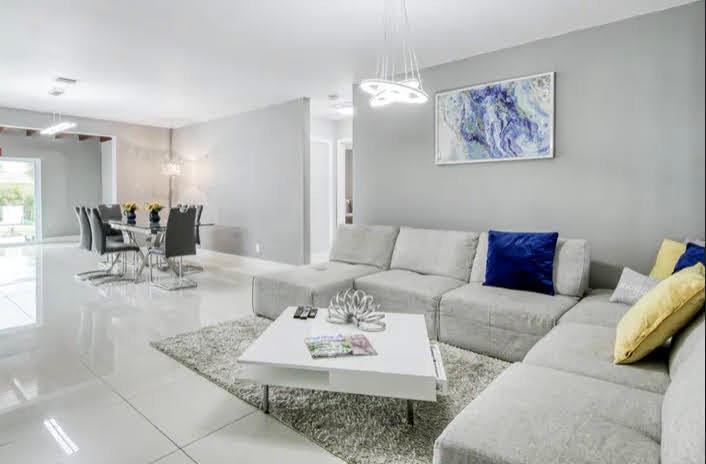 A modern living room with a gray sectional sofa, white coffee table, and adjacent dining area — 1905 N 45th Avenue, Hollywood FL 33021, HOLLYWOOD, FL