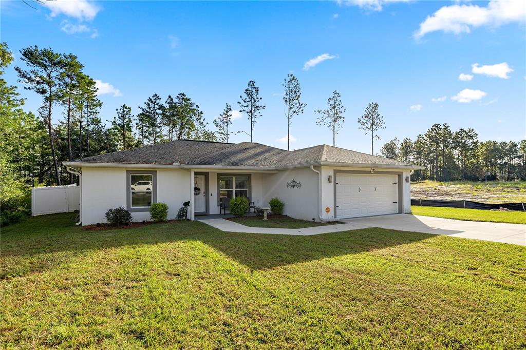 A single-story white house with a two-car garage sits on a grassy lot — 8607 SW 135TH STREET ROAD, OCALA, FL