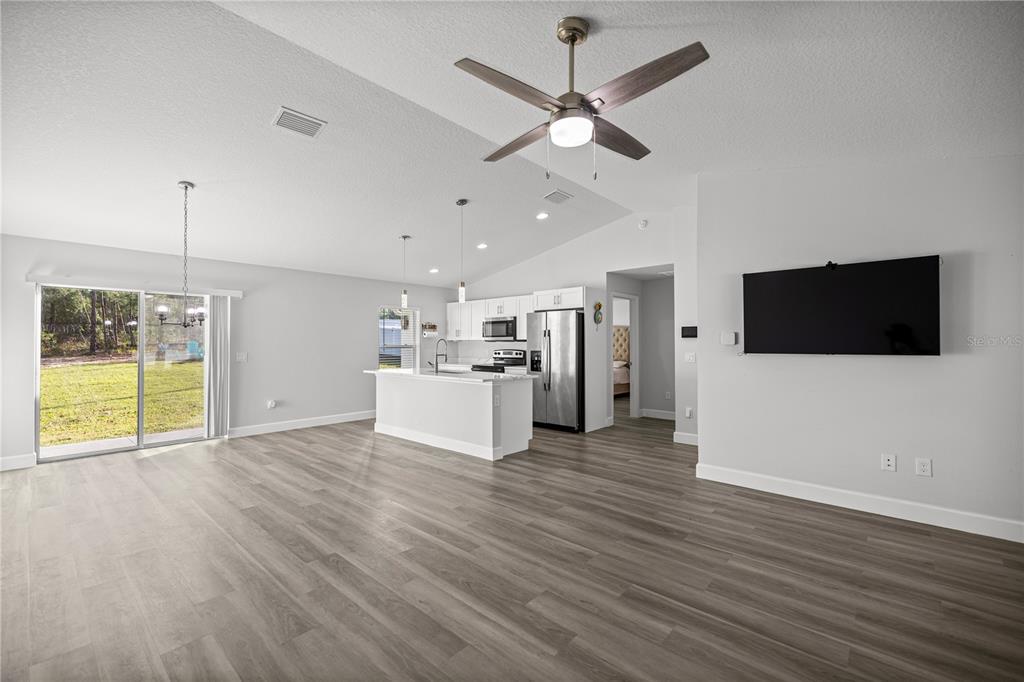 An open-concept living area features light wood-look flooring, a kitchen island, and a ceiling fan — 8607 SW 135TH STREET ROAD, OCALA, FL