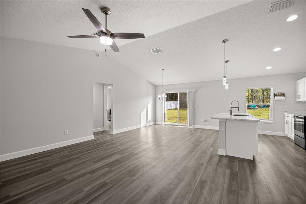 An open-concept kitchen and living area with light gray walls and wood-look vinyl flooring — 8607 SW 135TH STREET ROAD, OCALA, FL
