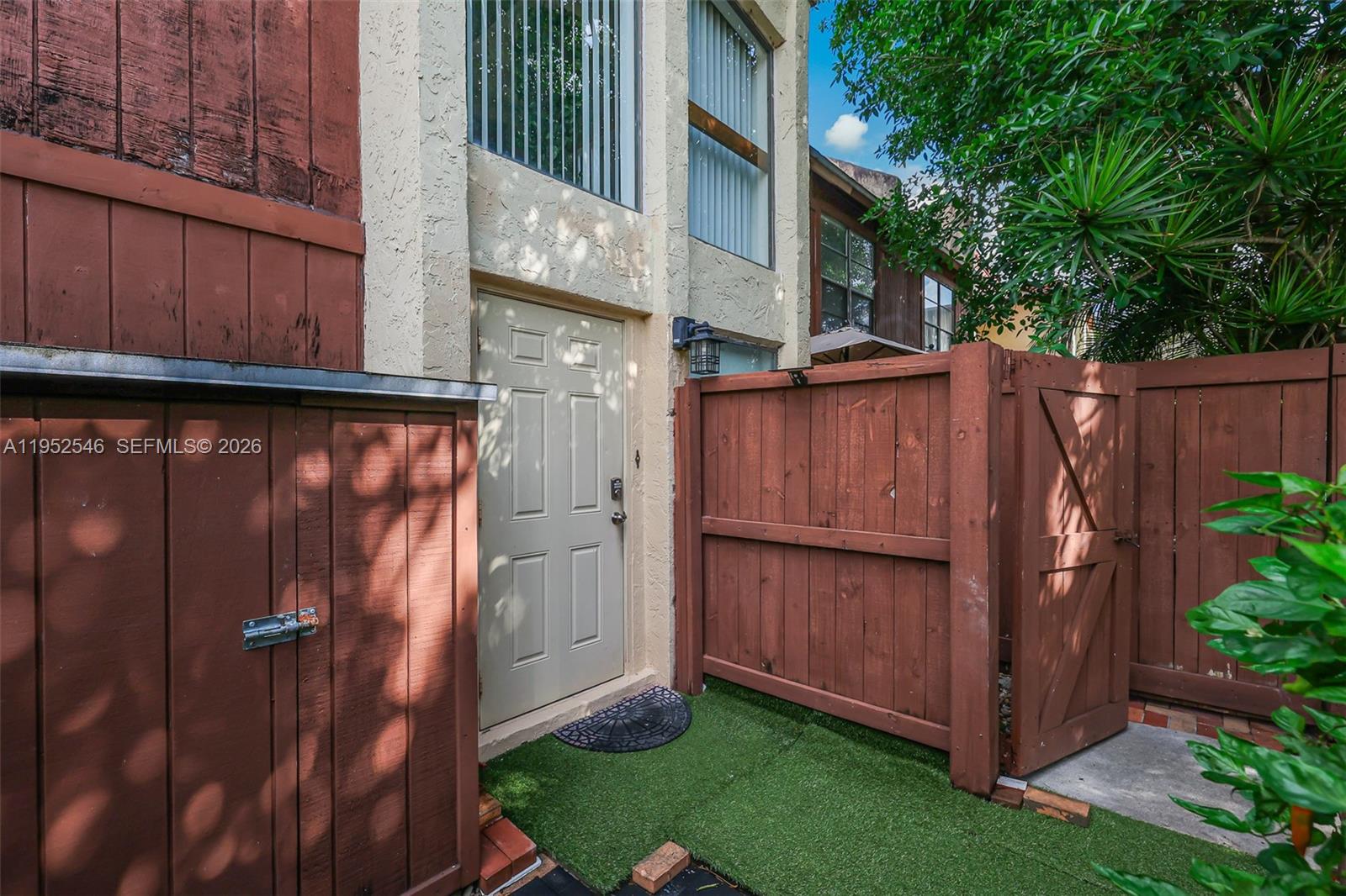 An exterior view of a building entrance with a wooden fence and artificial grass — 7014 SW 114th Pl # C53, Miami FL 33173, MIAMI, FL