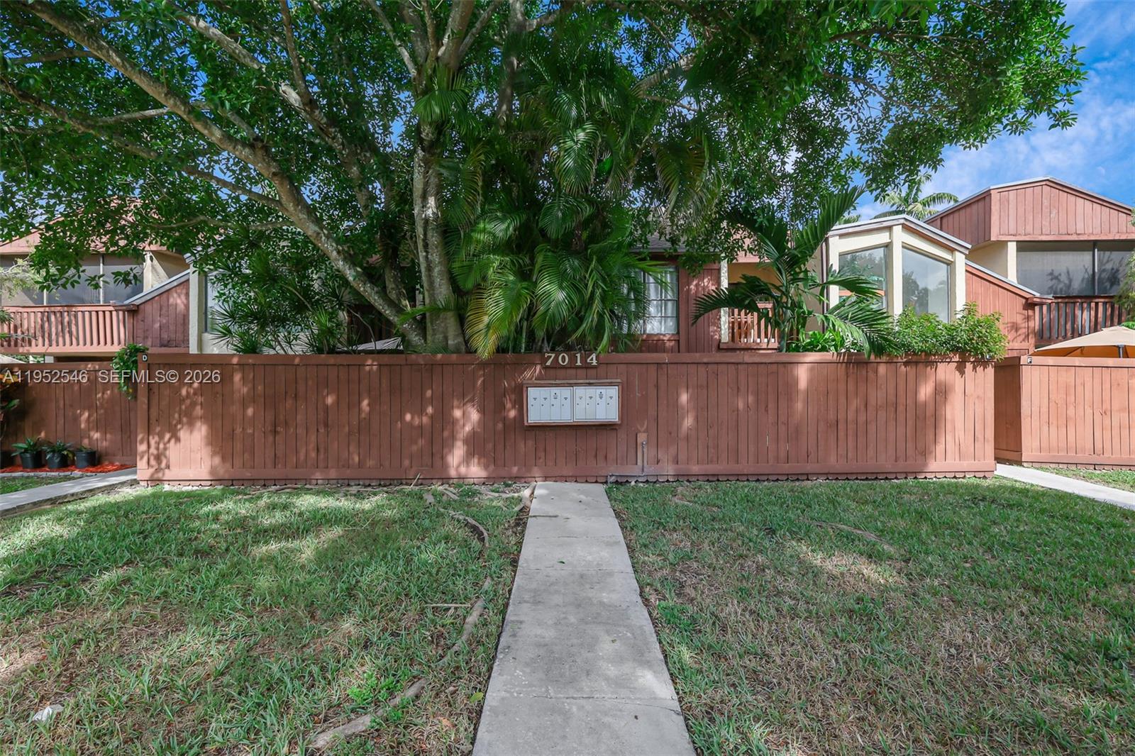 A wooden fence with a central mailbox unit stands before a multi-story residential building — 7014 SW 114th Pl # C53, Miami FL 33173, MIAMI, FL