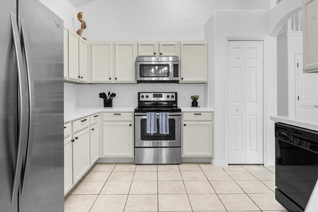 A kitchen features white cabinets, stainless steel appliances, white countertops, and light-colored tile flooring — 638 CASSIA DRIVE, DAVENPORT, FL