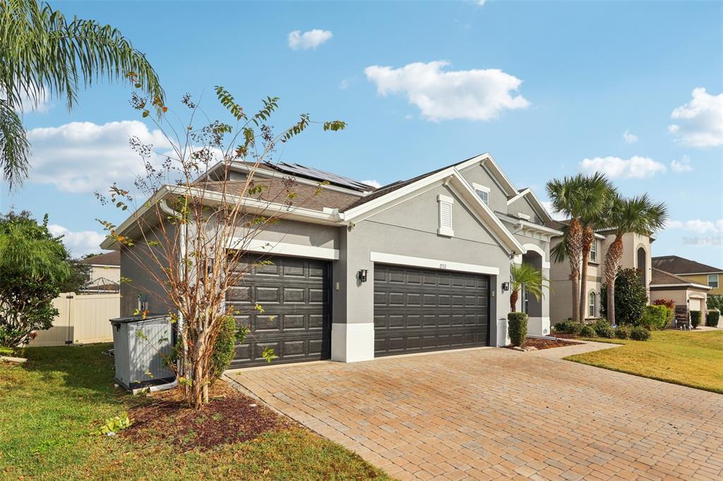 A gray house with a three-car garage and a paver driveway under a blue sky — 2132 PLANTATION OAK DRIVE, ORLANDO, FL
