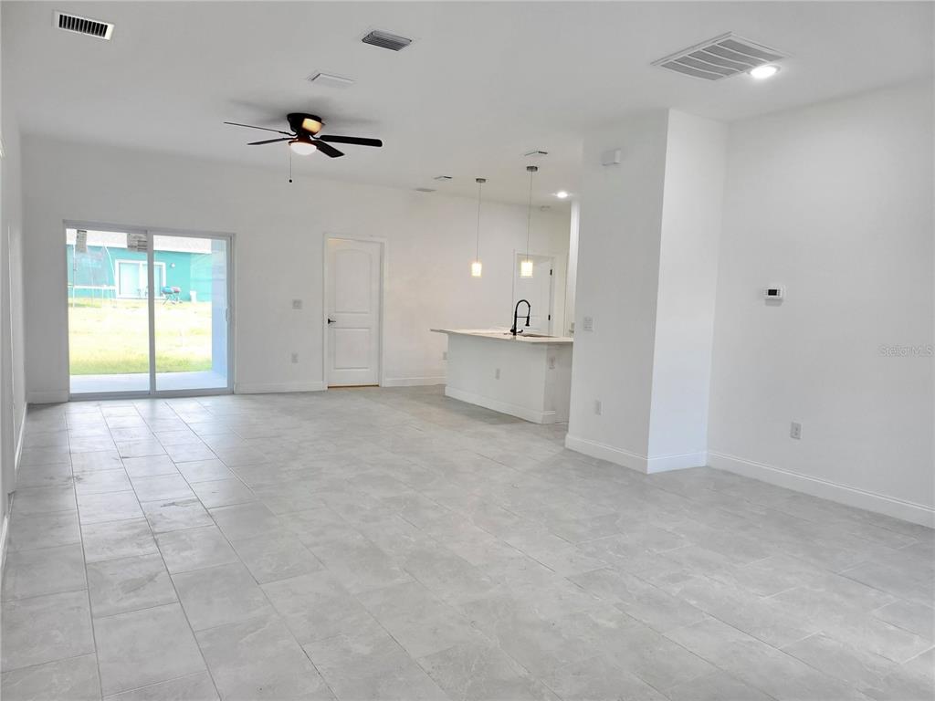 An open-concept living area features light gray tile flooring, a kitchen island, and sliding doors — 415 TONKLIN ROAD SW, PALM BAY, FL