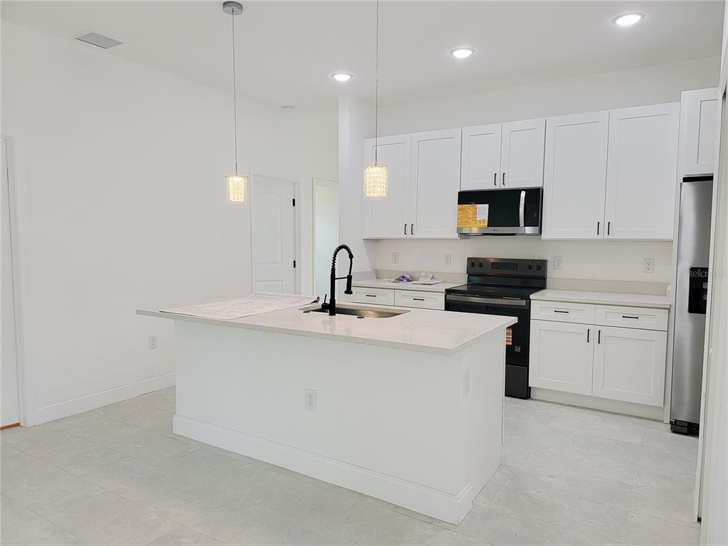 A modern kitchen features white cabinets, a central island with a sink, and stainless appliances — 415 TONKLIN ROAD SW, PALM BAY, FL