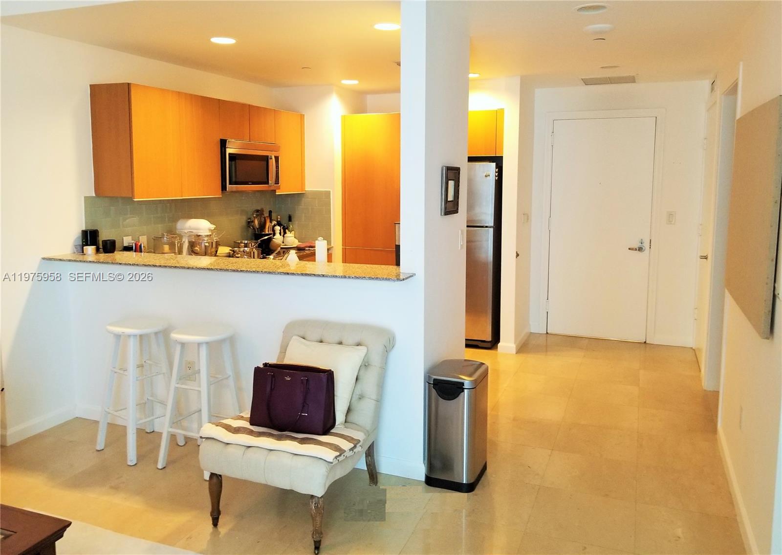 A kitchen with light wood cabinets and a breakfast bar overlooks a tiled living area — 1050 BRICKELL AV # 2622, Miami FL 33131, MIAMI, FL