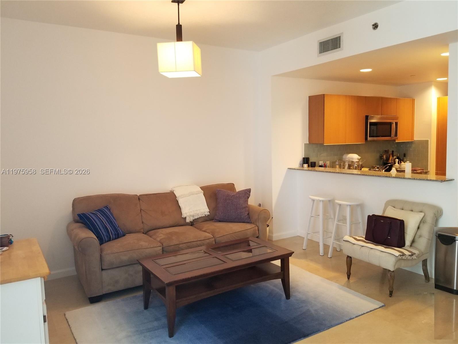 A living room with a brown sofa, coffee table, and an open kitchen with bar seating — 1050 BRICKELL AV # 2622, Miami FL 33131, MIAMI, FL